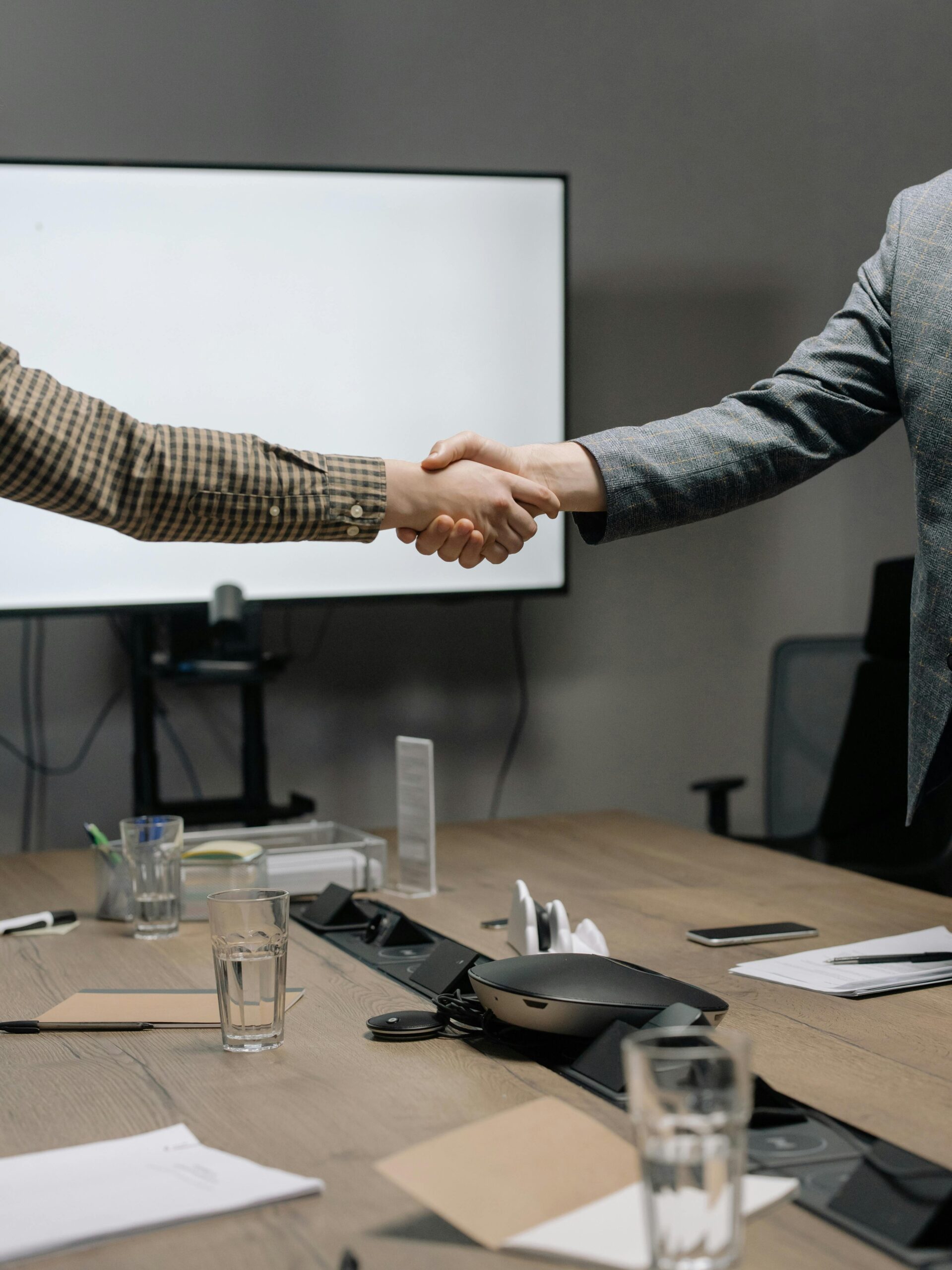 Two business professionals shaking hands in a modern meeting room, symbolizing successful collaboration.